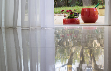 View From an Open Door of Room to Garden with Red Pots of Spring Flowers. Beautiful floor reflection of Sunny Day with Blue Sky. Concept: Spring & Gardening.