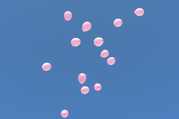 Group of pink balloons floating into a clear blue sky