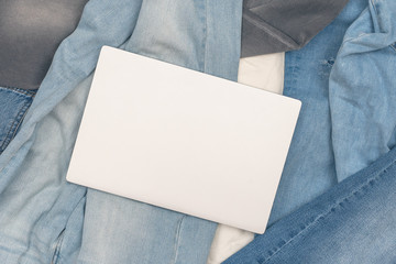 Laptop lying on the many different jeans scattered on the floor. Concept.