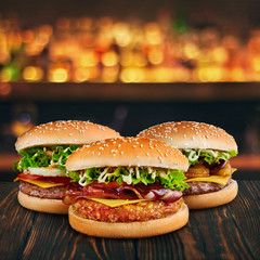 three burgers at brown wooden tabletop with blurred bar at backdrop . Fastfood concept with hamburgers at wooden table