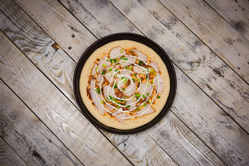 Round pizza dough is in the pan. The process of cooking pizza, stacking ingredients on the dough.