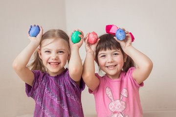 two happy cute babies sisters twins 6-7 years old paint Easter eggs, laugh, make faces