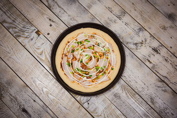 Round pizza dough is in the pan. The process of cooking pizza, stacking ingredients on the dough.
