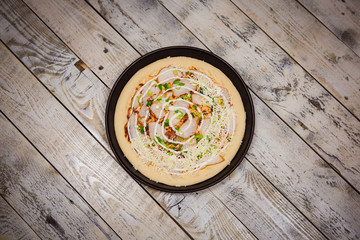 Round pizza dough is in the pan. The process of cooking pizza, stacking ingredients on the dough.
