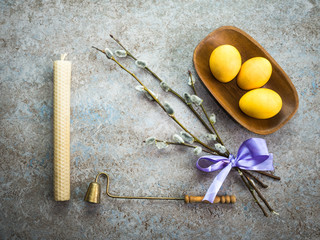 Happy Easter greeting card. Colored Easter eggs in wooden plate, wax candle, brass extinguisher and willow branches on the stone background. Easter concept.