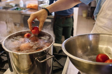A man puts a tomato in a pot of boiling water. The process of making tomato sauce. Tomatoes in a pot of boiling water