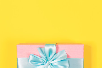 Pink gift box tied with blue ribbon with bow at the top on yellow background. Copy space for text. Minimal flat lay. Top view. Birthday, New year, Mother's day, Women's day celebration concept.