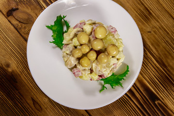 Potato salad with marinated mushrooms, sausage, onion and mayonnaise on wooden table
