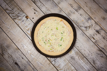 Round pizza dough is in the pan. The process of cooking pizza, stacking ingredients on the dough.