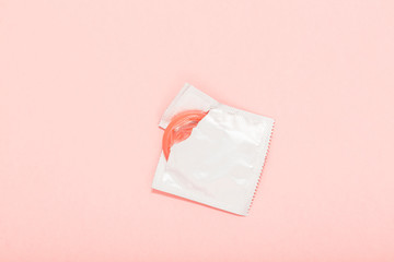 Pink opened condom and condom in pack on a pink background. A condom use to reduce the probability...