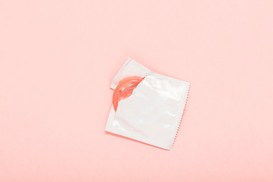 Pink opened condom and condom in pack on a pink background. A condom use to reduce the probability of pregnancy or sexually transmitted disease (STD). Safe sex and reproductive health concept.