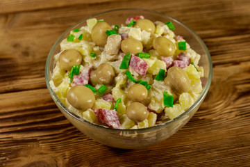 Potato salad with marinated mushrooms, sausage, onion and mayonnaise on wooden table