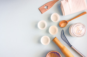 Fototapeta na wymiar Culinary background. Cooking utensils, a whisk, a rolling pin, cupcake pans, a wooden bowl and baking ingredients. Bakery background frame. Top view, copy space.