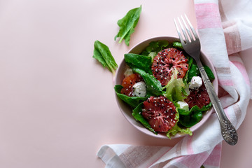 Spring fresh salad with blood orange, lettuce, spinach and sesame seeds on pink background. Top view. Selective focus