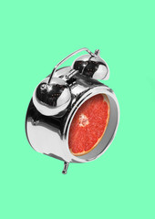 It's time for vitamins. An alarm or clock with juicy red grapefruit or citrus in centre against light mint background. Negative space to insert your text. Modern design. Contemporary art collage.