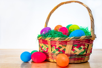 Easter basket with colorful plastic Easter eggs. Vintage woven wicker egg hunt basket, green grass, and vibrant colored classic eggs.