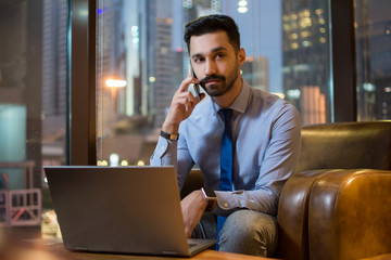 Young business man with laptop talking on mobile phone in modern office