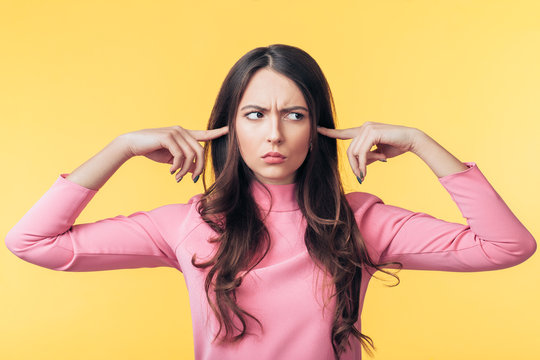 Beautiful offended woman covering her ears with fingers isolated on yellow background