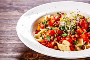 Pasta with tomato sauce and vegetables on wooden table