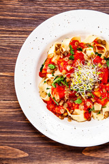 Pasta with tomato sauce and vegetables on wooden table