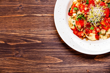 Pasta with tomato sauce and vegetables on wooden table