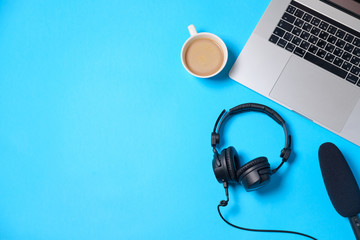 Music or podcast background with headphones, microphone, coffee and laptop on blue table, flat lay. Top view, flat lay