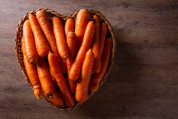 Many of carrots bunch in the heart basket on wooden background