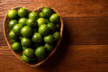 Fresh limes in a heart bowl on wooden table background. Top view.