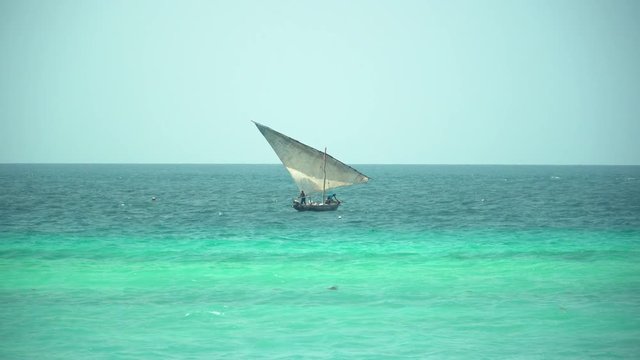 Man working on traditional african wooden dhow boat that swinging on the waves of bright turquoise ocean on sunny day. Zanzibar, Tanzania, Africa.