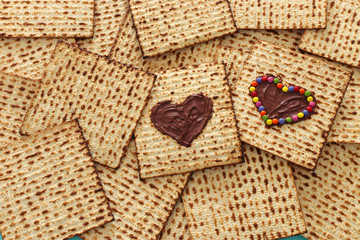Pesah celebration concept (jewish Passover holiday) with chocolate heart and colorful candies over matzah. Top view flat lay