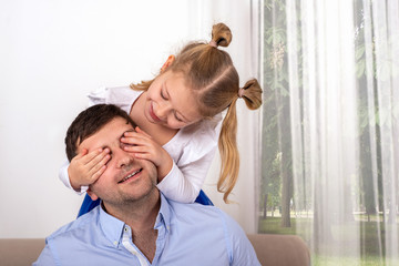 A little girl  is having fun playing with her dad, closing his eyes so that he can guess who it is.