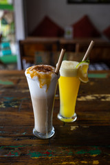 Freshly squeezed orange juice and chocolate milkshake in a tall glasses with a straw on a wooden vintage table in cafe. Copy space