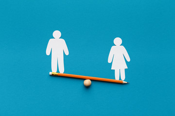 Female figure outweigh male on seesaw, blue background