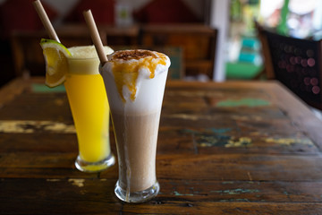 Freshly squeezed orange juice and chocolate milkshake in a tall glasses with a straw on a wooden vintage table in cafe. Copy space