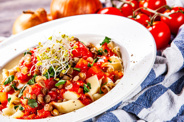 Pasta with tomato sauce and vegetables on wooden table