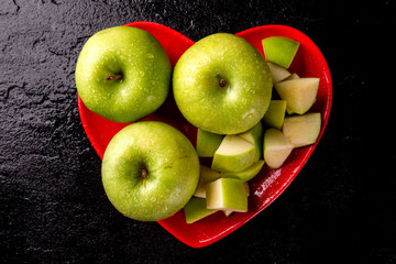 Ripe green apples into heart bowl on table close up.
