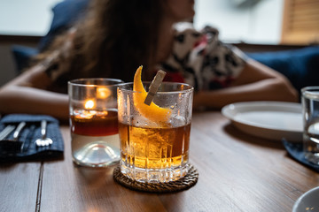 Old fashioned cocktail served in a whiskey glass at the restaurant. Woman in soft focus in the back ground. Copy space