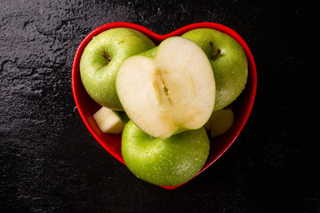 Ripe green apples into heart bowl on table close up.
