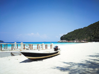 A boat is located by the beach in a tropical island beach with ombre sea in the background.