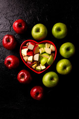 Ripe red and green apples into heart bowl on table close up.