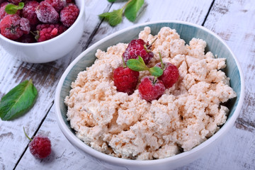 Cottage cheese topped with raspberries in a bowl on white wooden table