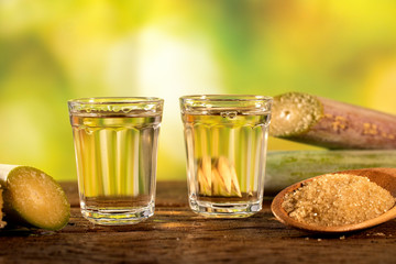 two shot glasses of Brazilian gold  cachaca with sugar and sugarcane isolated on rustic wooden background