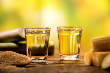 two shot glasses of Brazilian gold  cachaca with sugar and sugarcane isolated on rustic wooden background