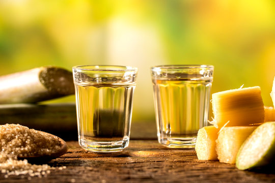 two shot glasses of Brazilian gold  cachaca with sugar and sugarcane isolated on rustic wooden background