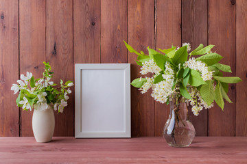 Mockup with a white frame and white spring flowers in a vase on a wooden table