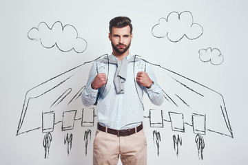 I am superhero. Confident and handsome man wearing a drawn flying cape while standing against grey background with illustration of the clouds on it.