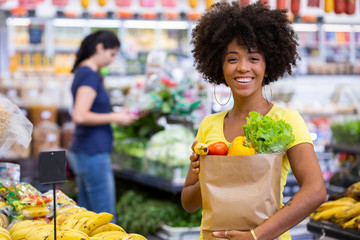 Healthy positive happy african woman holding a paper shopping bag full of fruit and vegetables