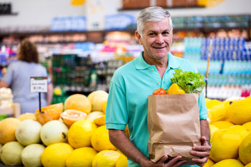 Healthy positive happy brazilian man holding a paper shopping bag full of vegetables.