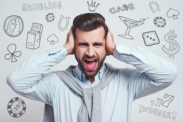 How could I loose? Young handsome man closing ears with hands and screaming while standing against grey background with different doodle illustrations on it. Gambling concept