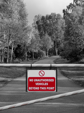 Monochrome Aufnahme Strasse mit B&auml;umen durch Wald mit Schranke und rotem Verbots Schild "no unauthorized vehicles beyond this point" 